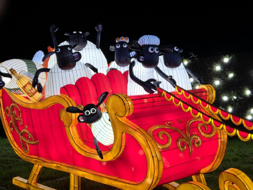 A lantern display at the Longleat Festival of Light, featuring Shaun the Sheep characters in a red sled, one sheep driving and others looking playful.